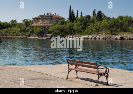 Banc traditionnel en bois sur les rives de la baie de la mer Adriatique. Ruines de l'autre côté de l'ancien hôtel, maintenant abandonnée. Les arbres et arbustes autour. Omisal Banque D'Images