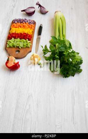 Les légumes frais, haché (carotte, céleri, oignon, poivrons de couleur) disposés sur une planche à découper sur la table en bois blanc, vue de côté. Copier l'espace. Banque D'Images