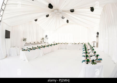 L'intérieur de tente pour diner de mariage, prêts pour les clients. Servi en plein air table de banquet ronde décorée de renom dans l'hydrangea fleurs, des plats d'or et vert. Concept de restauration Banque D'Images