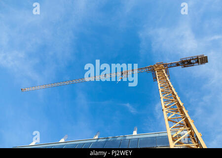 Le métal jaune en face de la grue d'un bâtiment en cours d'assemblage dans un chantier de prises d'en dessous lors d'un après-midi ensoleillé, sous un ciel bleu Photo Banque D'Images