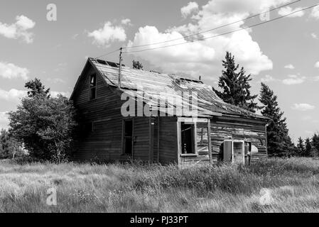 Ancienne ferme des prairies entourées d'arbres, d'herbes hautes et ciel de la Saskatchewan, le Canada en noir et blanc Banque D'Images