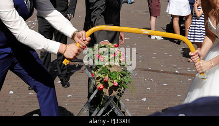 Les jeunes couples nuptiales scier un tronc d'arbre décoré avec des roses, Allemand tradition de mariage. Banque D'Images