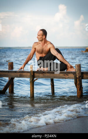 Les jeunes formateurs pratiquant de yoga ardha matsyendrasana ou seigneur des poissons posent sur une jetée en bois sur une rive de la rivière ou la mer. Concept de vie sain Banque D'Images