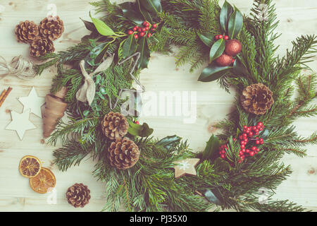 Photo aux couleurs de la couronne de Noël faites avec des branches de sapin, des pommes de pin, des baies, des babioles sur la table en bois naturel, haut vew, selective focus Banque D'Images