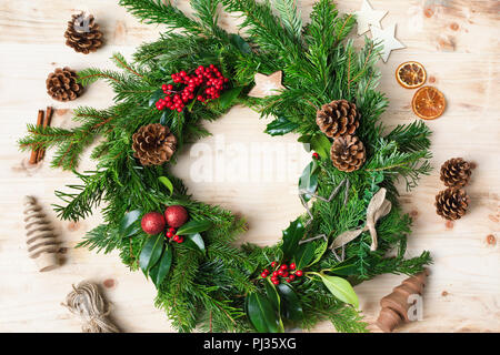 Couronne de Noël fait main décoration faite avec des branches de sapin, des pommes de pin, des baies, des babioles sur la table en bois naturel, haut vew, selective focus Banque D'Images