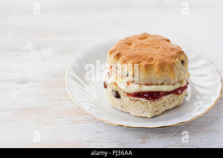 Un scone avec de la confiture et de la crème, sur la plaque, sur la table en bois blanc, portrait, Close up, copier du texte pour l'espace Banque D'Images