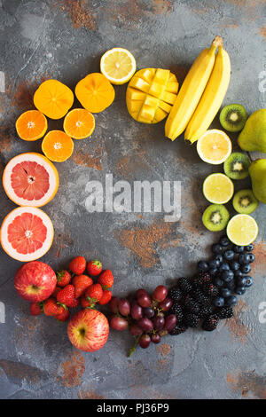 Fruits de couleur arc-en-ciel dans un cercle, fraises, bleuets, mangue, orange, pamplemousse, banane, pomme, raisins, kiwis, papayes sur le fond gris, Banque D'Images