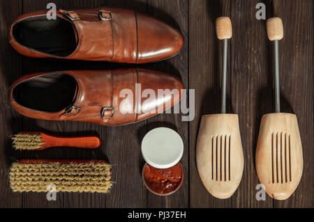 Chaussures en cuir avec des accessoires pour le nettoyage disposées sur une planche de bois Banque D'Images