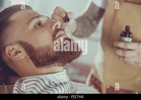 Le salon de coiffure s'applique l'huile barbe avec un compte-gouttes. Photo en style vintage Banque D'Images