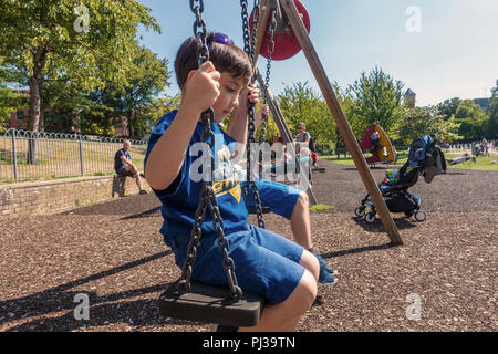 Un jeune garçon est assis sur une balançoire dans l'aire de jeux pour enfants dans la région de Bachelors acre à Windsor, Royaume-Uni. Banque D'Images