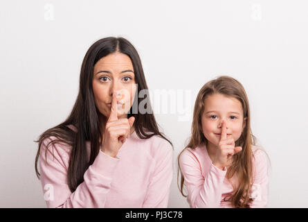 Une petite fille et sa mère dans un studio avec un doigt sur leurs lèvres. Banque D'Images