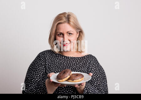 Une jolie femme en surpoids en studio, holding donuts sur une assiette. Banque D'Images