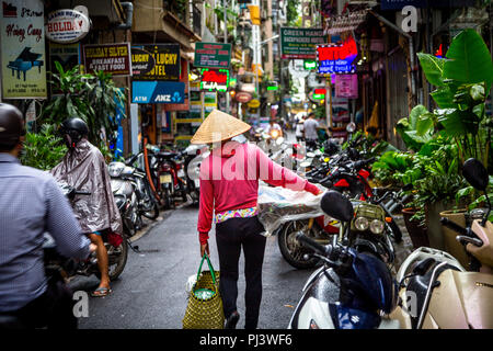 Ruelle bondée centrée sur dame asiatique wearing Hat et Red top et déposer quelque chose de marcher au milieu de l'allée. Compresse le téléobjectif Banque D'Images