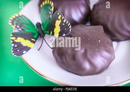 Sur un fond vert sur une assiette de guimauves recouverte de chocolat. Décoration suivant sous la forme d'un papillon. Banque D'Images