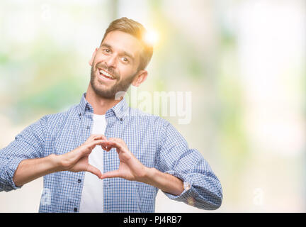 Beau jeune homme portant un t-shirt blanc sur fond isolé smiling in love montrant le symbole de coeur et la forme des mains. Concept romantique. Banque D'Images