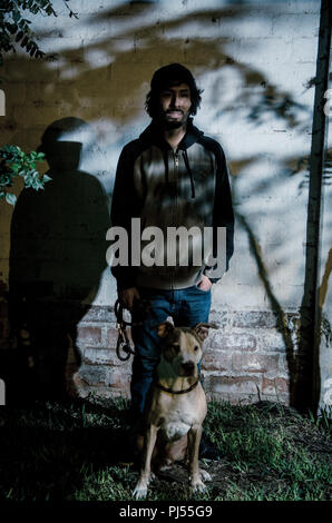 Portrait de jeune homme barbu avec chemise et abat des arbres dans le parc avec pitbull dog Banque D'Images