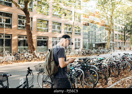 Un étudiant avec un sac à dos ou un touriste sur la rue de Leipzig en Allemagne utilise un téléphone cellulaire à côté du parking à vélos qui est à côté de la bibliothèque de l'Université de Leipig et student hostel. Banque D'Images