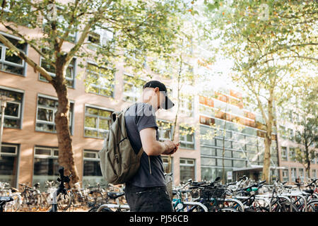 Un étudiant avec un sac à dos ou un touriste sur la rue de Leipzig en Allemagne utilise un téléphone cellulaire à côté du parking à vélos qui est à côté de la bibliothèque de l'Université de Leipig et student hostel. Banque D'Images