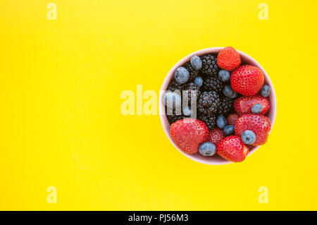 Bol Rose avec plein de petits fruits fraîchement cueillis sur fond jaune. Banque D'Images