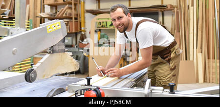 Friendly carpenter avec protège-oreilles et des vêtements de travail travaillant sur une scie dans l'atelier Banque D'Images