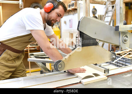 Friendly carpenter avec protège-oreilles et des vêtements de travail travaillant sur une scie dans l'atelier Banque D'Images