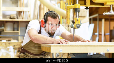 Friendly carpenter avec protège-oreilles et des vêtements de travail travaillant sur une scie dans l'atelier Banque D'Images