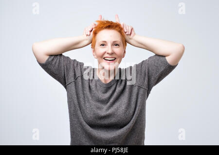 Élégante maturité expressive femme aux cheveux rouges avec un clin d'griffes flirty et derrière la tête comme Bunny Ears Banque D'Images