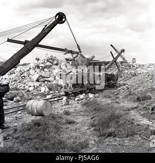 Années 1950, le déplacement de grandes chargeuses mécaniques des roches calcaires du bord d'une carrière en langue étroite de wagons de fret ferroviaire ouvert, England, UK. Banque D'Images