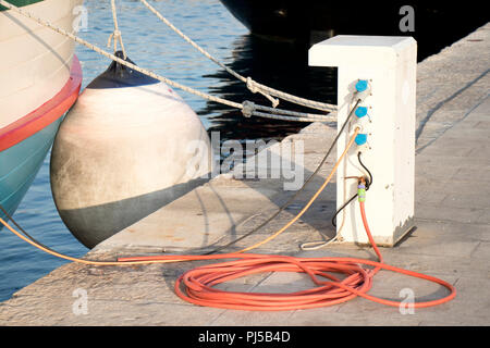 Pier avec commande électrique et l'approvisionnement en eau avec socle et câble flexible , bitt et une corde sur le dock attaché à un bateau vintage avec fender Banque D'Images