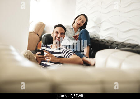 Jeune homme et femme avec la messagerie des téléphones mobiles sur canapé à la maison. Heureux couple l'utilisation de téléphones cellulaires. Les gens using smartphones Banque D'Images