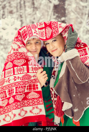 Jeune couple, homme et femme, mari et femme sont en marche les costumes de fleurs typiques des elfes de Santa's helpers dans une forêt d'hiver sous la neige avec un coffre plein de cadeaux et d'un bonbon géant Banque D'Images