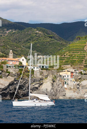 White voilier ancré au large de la côte du parc national des Cinque Terre en Italie, vous pouvez voir les vignes sur les pentes et d'un petit village Banque D'Images