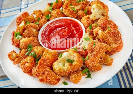 Chou-fleur pané cuit délicieux saupoudré de persil finement haché sur une plaque blanche avec de la sauce tomate, vue de dessus, close-up Banque D'Images