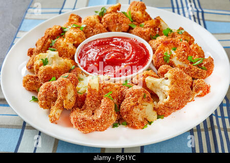 Close-up of delicious chou-fleur pané cuit au four saupoudré de persil finement haché sur une plaque blanche avec de la sauce tomate, vue de dessus Banque D'Images