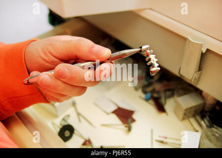 Des mains, c'est tenant une couronne dentaire métallique en acier. Prothèses dentaires, prothèses dentaires, prothèses travail. Technicien dentaire en processus de fabrication de prothèses dentaires. Banque D'Images