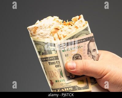 Shawarma dans la main d'un homme enveloppé dans dollar bills Banque D'Images