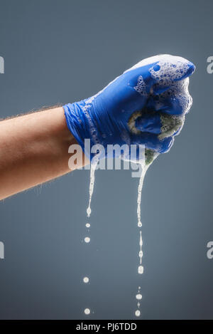 La main des hommes en bleu gant avec mousse dégoulinant Banque D'Images