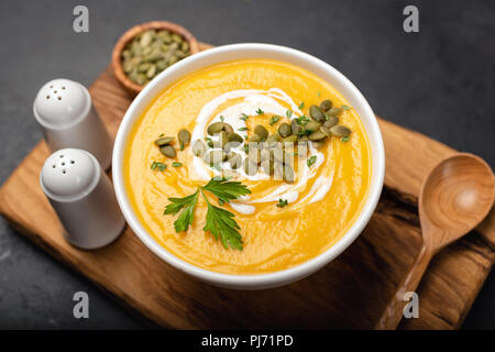 Crème de potiron soupe garnie de crème fraîche et graines de citrouille sur le service à bord. Vue rapprochée, selective focus Banque D'Images