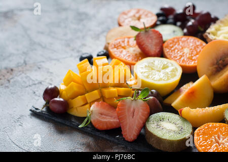 Petit-déjeuner végétalien, fruits et baies close up, tranché sur le fond noir en gris, copiez l'espace. Ananas, mangue, satsuma, kiwis, pêches, oranges, stra Banque D'Images
