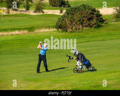 Man avec chariot de golf club de golf oscillante de frapper sur une balle de golf parcours de golf en soleil, Édimbourg, Écosse, Royaume-Uni Banque D'Images