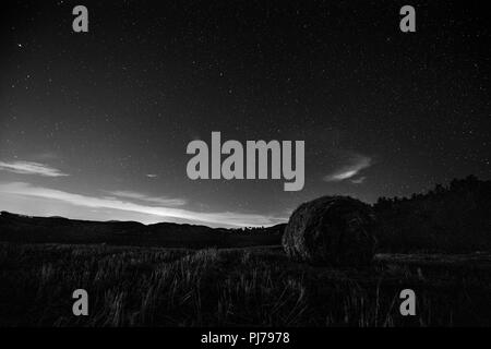 Belle Vue de nuit étoilé ciel avec nuages sur un champ cultivé avec des balles de foin Banque D'Images