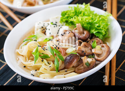 Soupe de nouilles au tofu vegan cheese, les champignons shiitake et de laitue dans un bol blanc. La cuisine asiatique. Banque D'Images