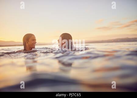 Jeune couple swimming in ocean at sunset Banque D'Images