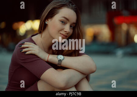 Belle jeune fille solitaire de rêver et penser, jeune femme posant dans la rue de la ville avec des bâtiments et des feux à l'arrière-plan. Banque D'Images