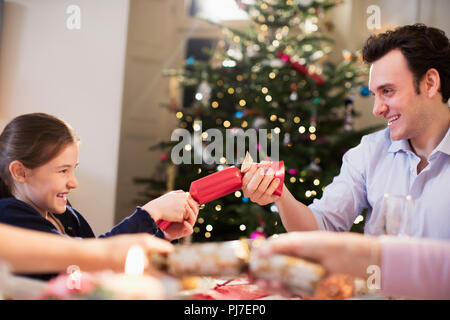 Père et fille pulling Christmas Cracker at dinner table Banque D'Images