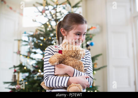 Happy girl hugging teddy bear in front of Christmas Tree Banque D'Images