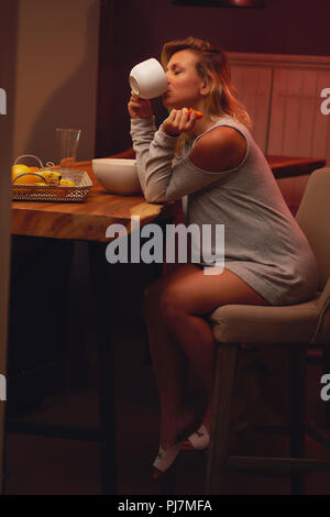 Jeune femme enceinte assis et boire un thé, café dans la cuisine à la maison Banque D'Images