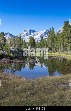 Un petit lac de montagne sans nom reflète les sommets de montagnes lointaines et arbres dans ce paysage magnifique des montagnes de la Sierra Nevada en Californie Banque D'Images