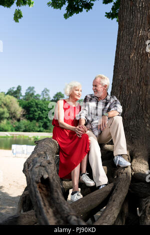 Couple de retraités aimant mignon assis sur grand arbre près de belle rivière Banque D'Images