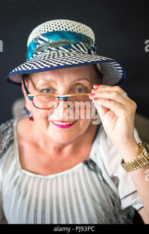 Élégant femme âgée assise sur le fauteuil avec fond noir Banque D'Images